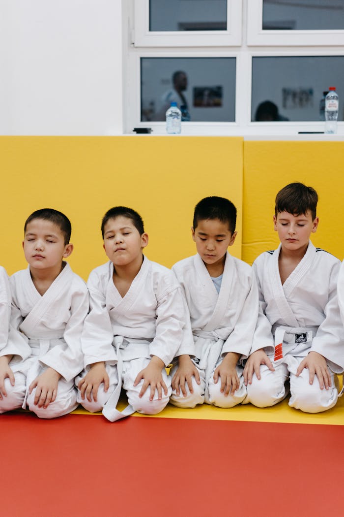 Young boys in judo uniforms meditating in a dojo, eyes closed in focus during training session.