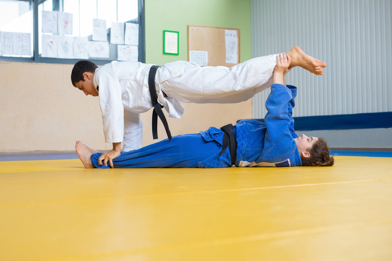 Two martial artists practicing judo techniques in an indoor dojo setting.